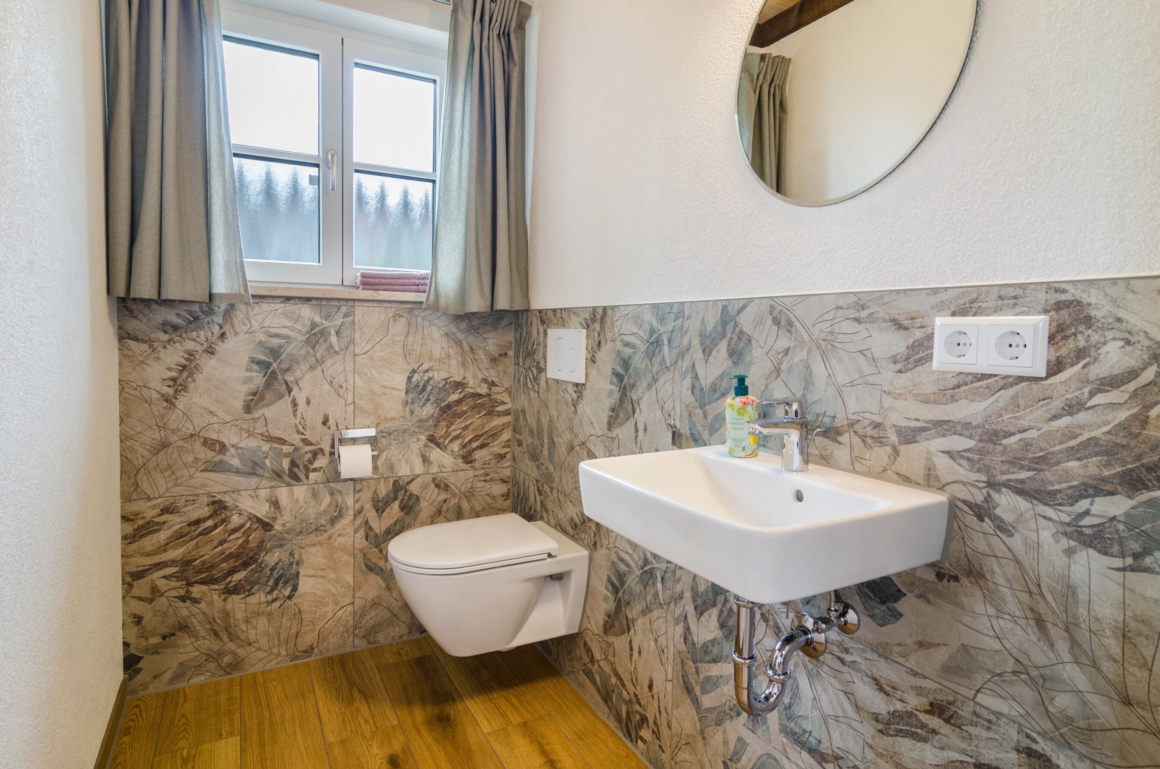 A bathroom with a toilet, sink, and window with curtains.