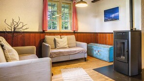Un salon avec un canapé, une commode bleue, une cheminée et une fenêtre ornée de rideaux rouges.