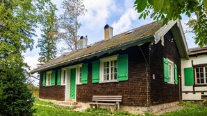 Una casa de madera tradicional con contraventanas verdes, una banca afuera y un cielo despejado.