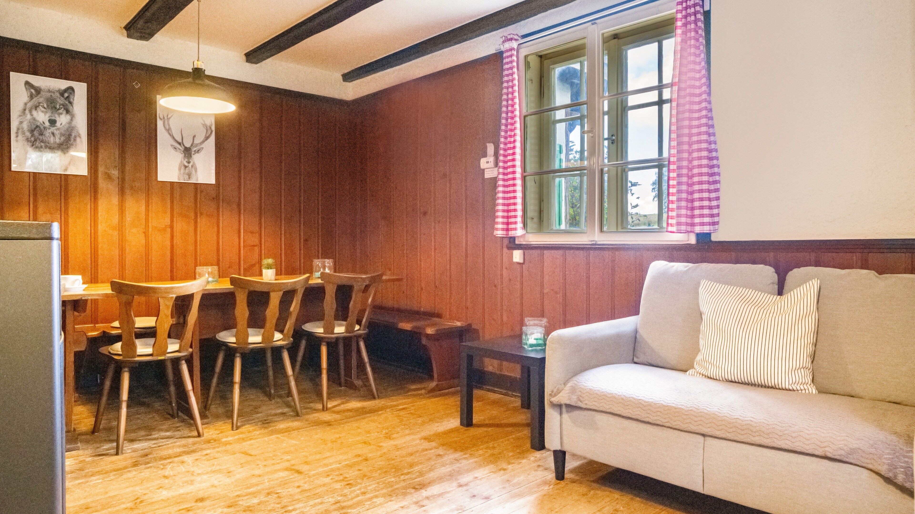 Une pièce chaleureuse aux murs en bois, avec une table à manger et des chaises, un canapé et une fenêtre agrémentée de rideaux.