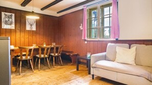 Une pièce chaleureuse aux murs en bois, avec une table à manger et des chaises, un canapé et une fenêtre agrémentée de rideaux.