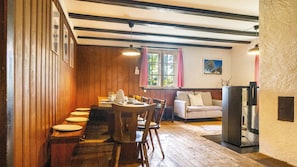 A dining area with wooden paneling, a table set for four, and a sofa in the background.