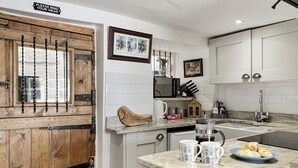A kitchen with white cabinets, a wooden door, and a marble countertop. - Captain's Cottage, Minehead (Minehead)