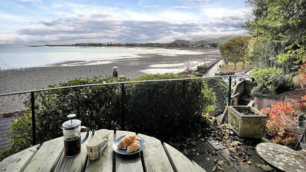 A wooden table with a plate of croissants and two cups, overlooking a beach with a rocky shoreline and a view of the sea and distant hills. - Captain's Cottage, Minehead (Minehead)