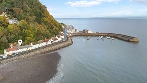 A coastal town with a rocky shoreline, a pier extending into the sea, and a road leading to a white building with a red roof. - Captain's Cottage, Minehead (Minehead)