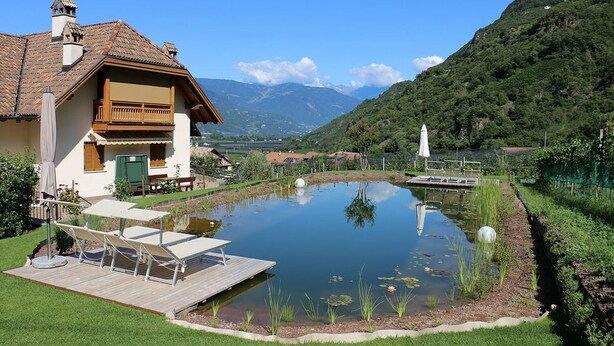 A house with a pond, deck, and mountain backdrop. - Holiday Apartment "Rosengartnerhof Maultasch" with Mountain View, Shared Pool & Wi-Fi (Terlan)