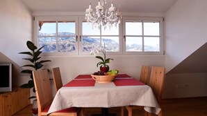 A dining area with a table set for four, a chandelier, and a view of mountains through large windows. - Holiday Apartment "Rosengartnerhof Maultasch" with Mountain View, Shared Pool & Wi-Fi (Terlan)