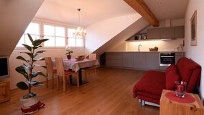 A dining area with a table and chairs, a potted plant, and a red sofa in a room with wooden flooring and a sloped ceiling. - Holiday Apartment "Rosengartnerhof Maultasch" with Mountain View, Shared Pool & Wi-Fi (Terlan)