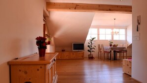 A spacious loft with high ceilings, wooden beams, a dining area with a table and chairs, and a TV on a wooden cabinet. - Holiday Apartment "Rosengartnerhof Maultasch" with Mountain View, Shared Pool & Wi-Fi (Terlan)