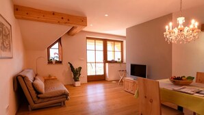 Una habitación con sofá, una mesa de comedor con sillas, una araña, televisión y ventana con vistas.