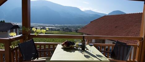 A wooden deck with a table set for two, overlooking a mountainous landscape.
