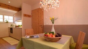 Un comedor con una mesa dispuesta para dos personas, un florero con flores y un cuenco de madera lleno de fruta.