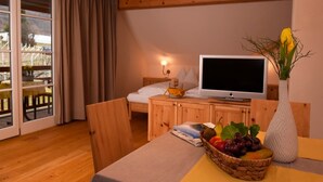 Een kamer met een bed, een televisie, een eettafel met een fruitmand en een vaas met bloemen.