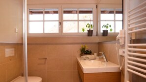 Een badkamer met toilet, wastafel en douche. Er staan planten op de vensterbank en een handdoekrek.