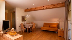 Een moderne woonkamer met een houten vloer, een bank, een eettafel met stoelen, een televisie op een houten dressoir en een kroonluchter.