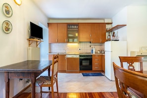 A compact kitchen with wooden cabinets, a built-in oven, a dishwasher, and a dining area with a table and chairs.