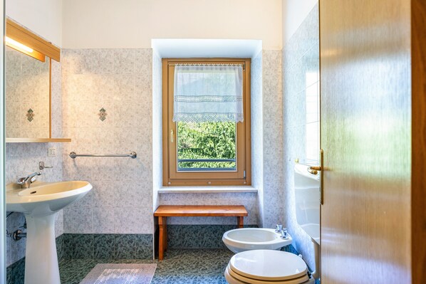 Un baño con un lavabo, dos inodoros, un banco, una ventana y un espejo.
