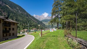 A road curving through a mountainous area with a building on the left and a fenced area with signs.