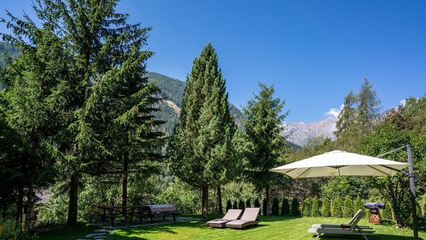 A backyard with a stone path, two lounge chairs, a picnic table, and a large umbrella.