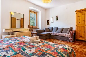 A bedroom with a bed, a sofa, a wooden wardrobe, a mirror, and a window.