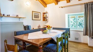Un comedor con una mesa de madera, sillas con estampado azul, un cuenco de fruta y una ventana con vistas a zonas verdes.