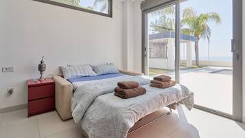 A bedroom with a bed, a nightstand, a lamp, and a view of the outside.