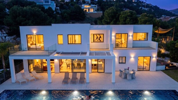 Una casa moderna de varios pisos con piscina, mobiliario exterior y vistas a las colinas circundantes.