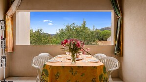 Un comedor con una mesa preparada para cuatro, un jarrón de flores y vista a un paisaje montañoso a través de una ventana.