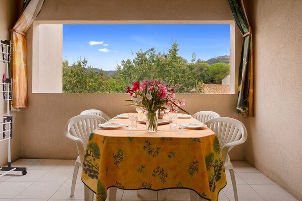 Un coin repas avec une table dressée pour quatre personnes, un vase de fleurs et une vue sur un paysage montagneux par la fenêtre.