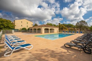 Un espace piscine avec des chaises longues, un coin salon abrité et un bâtiment en arrière-plan.
