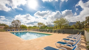 Una piscina con sillones de descanso, una terraza con baldosas y vistas a árboles y montañas.