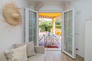 An open door leading to an outdoor patio with a table and chairs, a woven wall decoration, and a white sofa with cushions inside. - "Isabel Beach and Bike" Apartment with Private Garden and Wi-Fi (Finale Ligure)