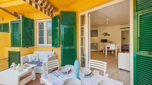 A dining area with a table set for four, a sofa, and a window with green shutters. - "Isabel Beach and Bike" Apartment with Private Garden and Wi-Fi (Finale Ligure)
