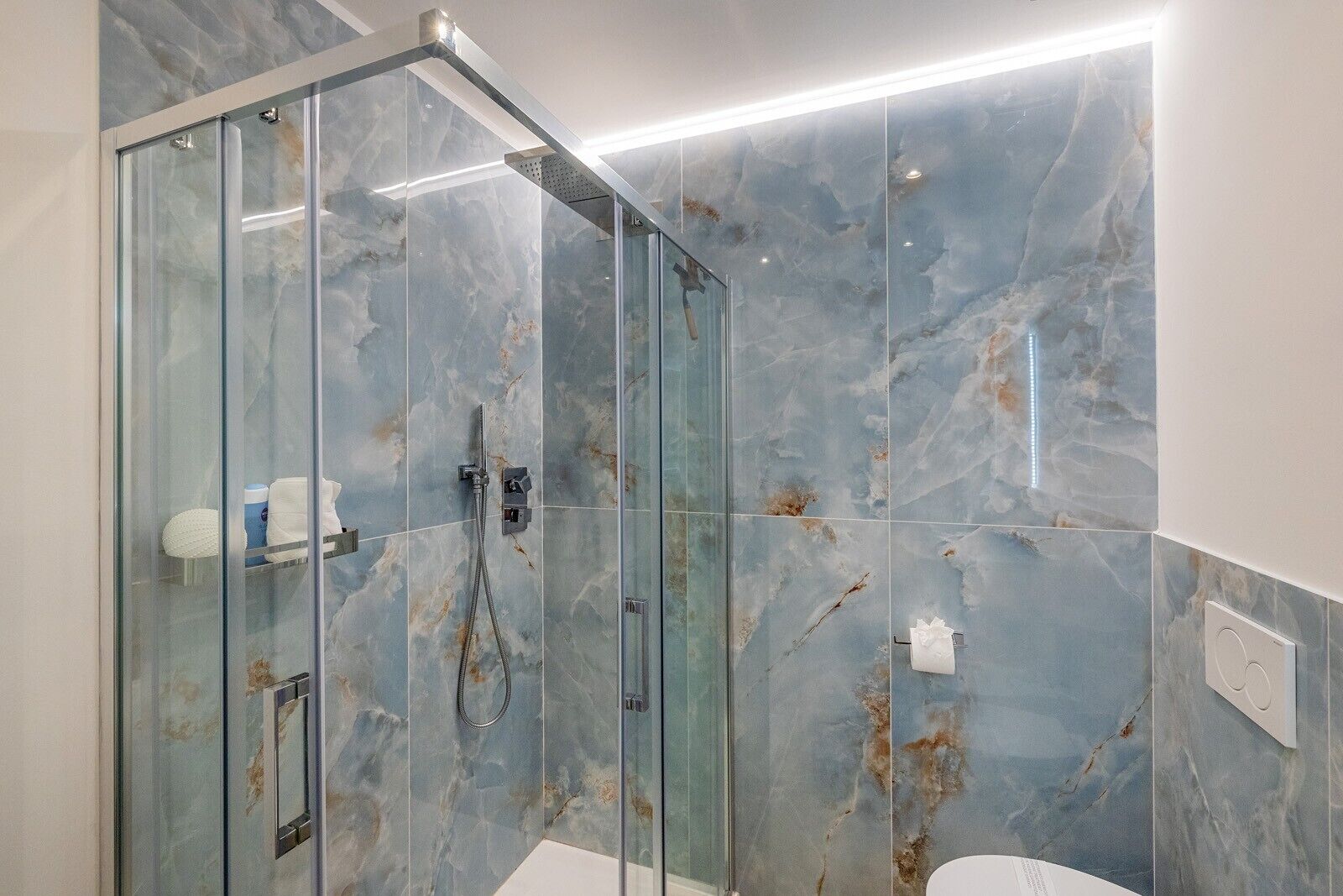 Ein modernes Badezimmer mit einer in Glas abgeschlossenen Dusche, Marmorfliesen und einem sichtbaren Toilettenpapierhalter.
