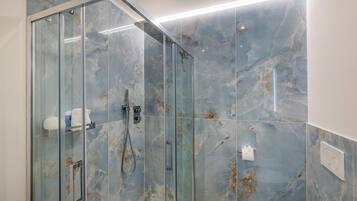 Ein modernes Badezimmer mit einer in Glas abgeschlossenen Dusche, Marmorfliesen und einem sichtbaren Toilettenpapierhalter.