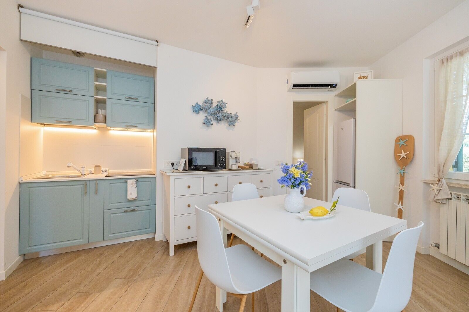 A compact kitchen with a microwave, a dining table with chairs, and a decorative wall piece.