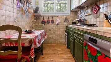 Een keuken met een eettafel, stoelen, een vaatwasser en een raam met uitzicht op bomen.