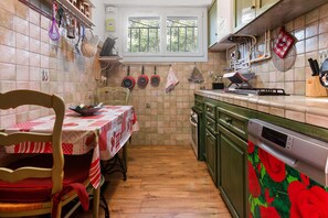 A kitchen with a dining table, chairs, a dishwasher, and a window with a view of trees. - Villa 'Sauvageonne' with Private Terrace, Wi-Fi and Air Conditioning (Saint Raphaël)