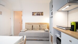 A compact kitchen with a dining area, a bed with patterned pillows, and a wall-mounted artwork. - Apartment "Aurisa" with Private Terrace & Wi-Fi (Bari)