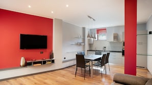 A modern kitchen with a dining area, a flat-screen TV mounted on the wall, and a red accent wall.
