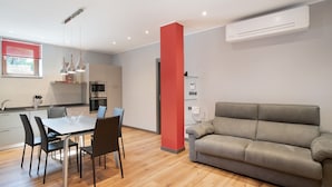 A modern kitchen with a dining table, chairs, and a grey sofa.