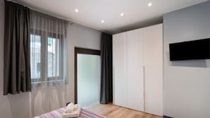 A modern bedroom with a bed, curtains, a television, and a wardrobe.