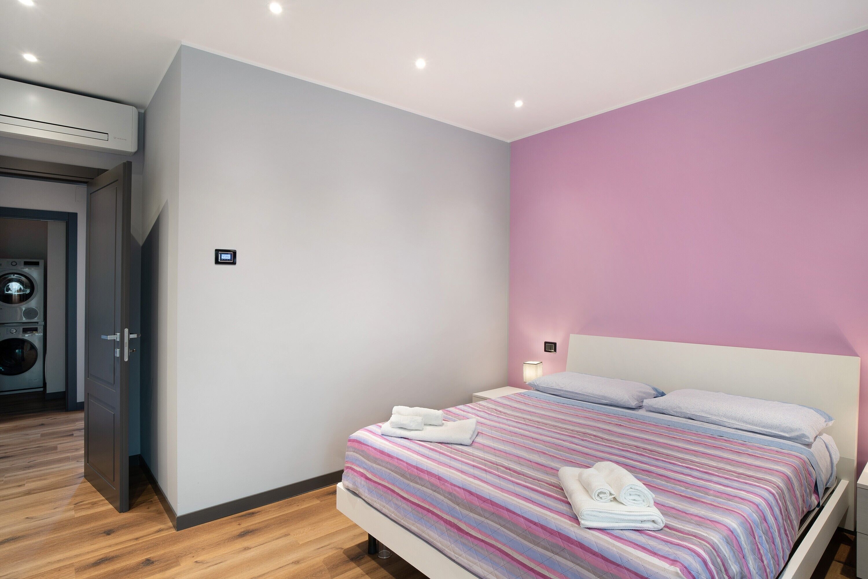 Quarto com cama, almofadas e toalhas. Há uma máquina de lavar no quarto vizinho.