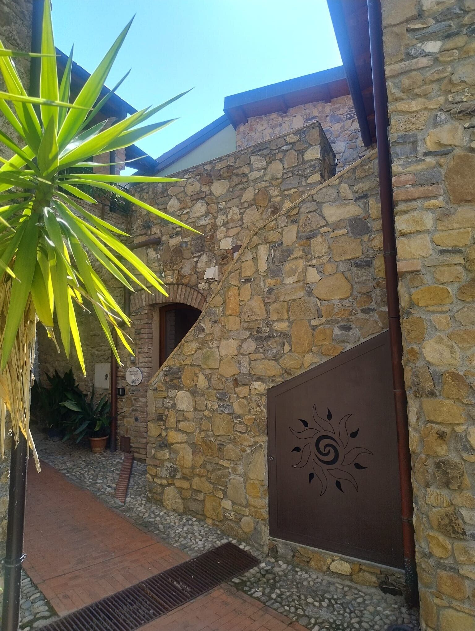 Un bâtiment en pierre avec une porte en métal, une plante en pot et un ciel dégagé.