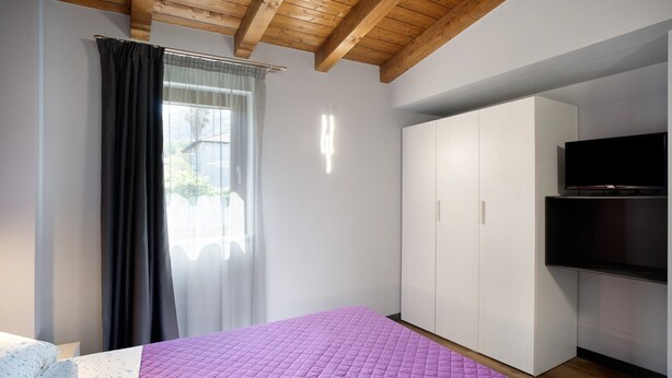 A bedroom with a bed, a wardrobe, a television, and a window with curtains. - Apartment "Agriturismo Il Borgo - Ulivo" with Private Terrace and Wi-Fi (Villanova d'Albenga)