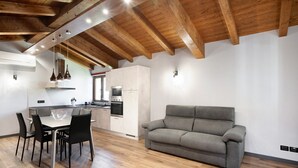 Eine moderne Küche mit Holzbalken, einem Esstisch mit Stühlen und einem grauen Sofa.