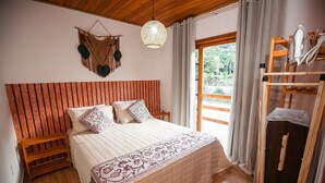 A bedroom with a wooden headboard, a bed with a patterned bedspread, a hanging light fixture, and a view of the outdoors through a window. - RSC02 Praia do Estaleito by ReservaStar (Balneário Camboriú)