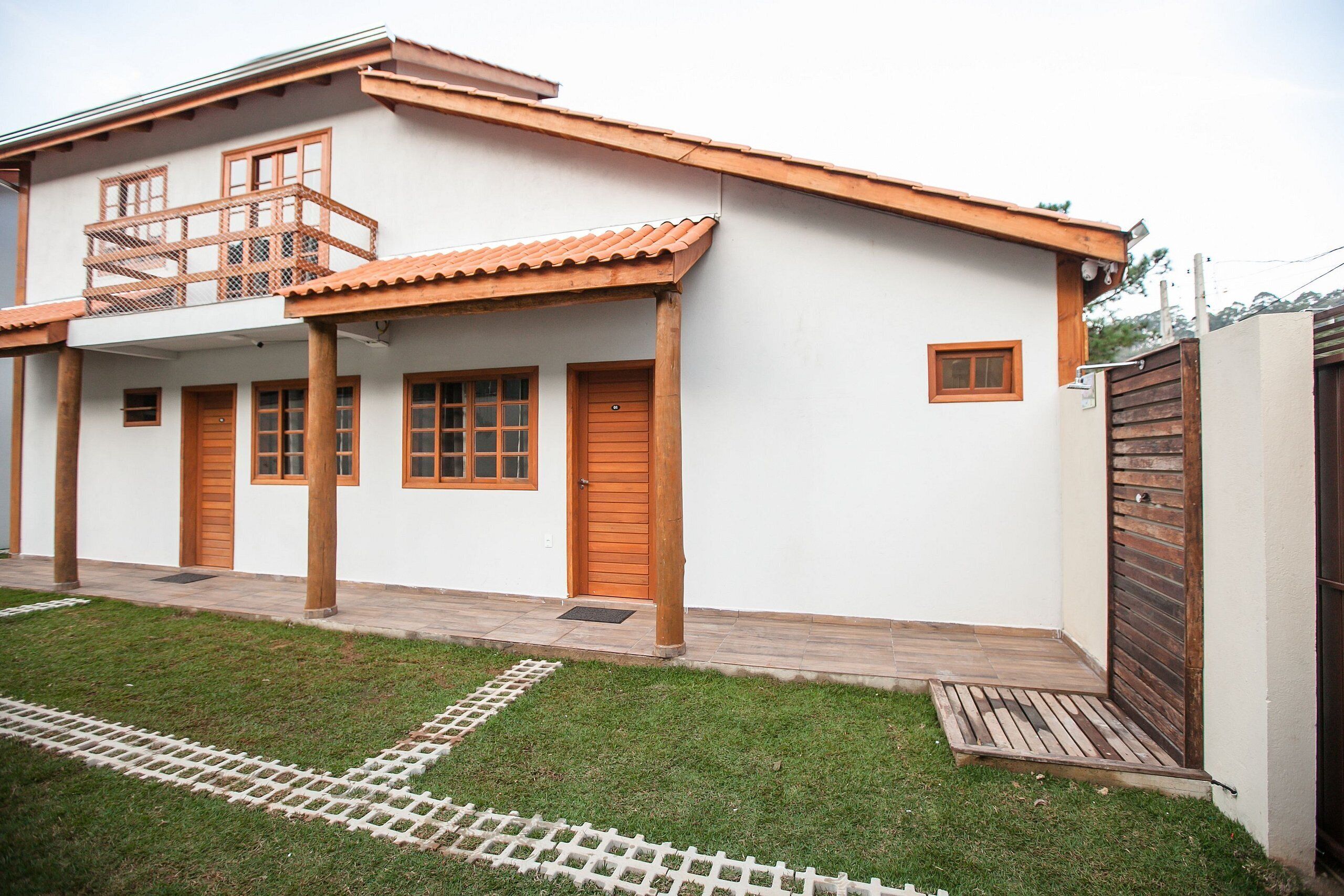 A two-story house with a balcony, wooden doors, and a small garden area.