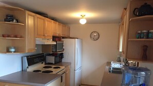 A compact kitchen with wooden cabinets, a stove, microwave, refrigerator, and a water dispenser.