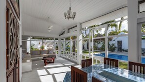 A spacious sunroom with a pool view, featuring a dining area with a table and chairs, a sofa, and a ceiling fan. - Walk to the beach & restaurants @ Las Terrenas for 10! (Las Terrenas)